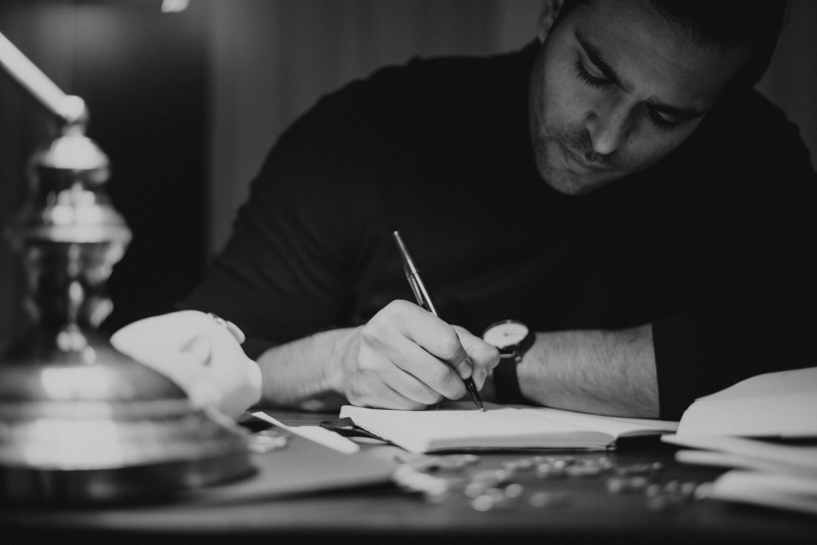 Zwartwit foto waar een man aan tafel in een boekje aan het schrijven is