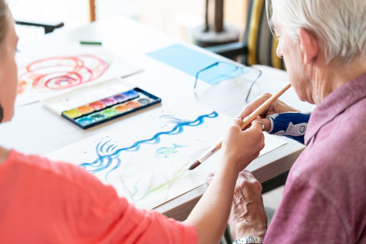 Kunstdocent helpt oudere met schilderen tijdens het project kunstknuffel