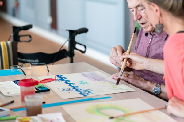 kunstdocent helpt oudere schilderen tijdens het project kunstknuffel