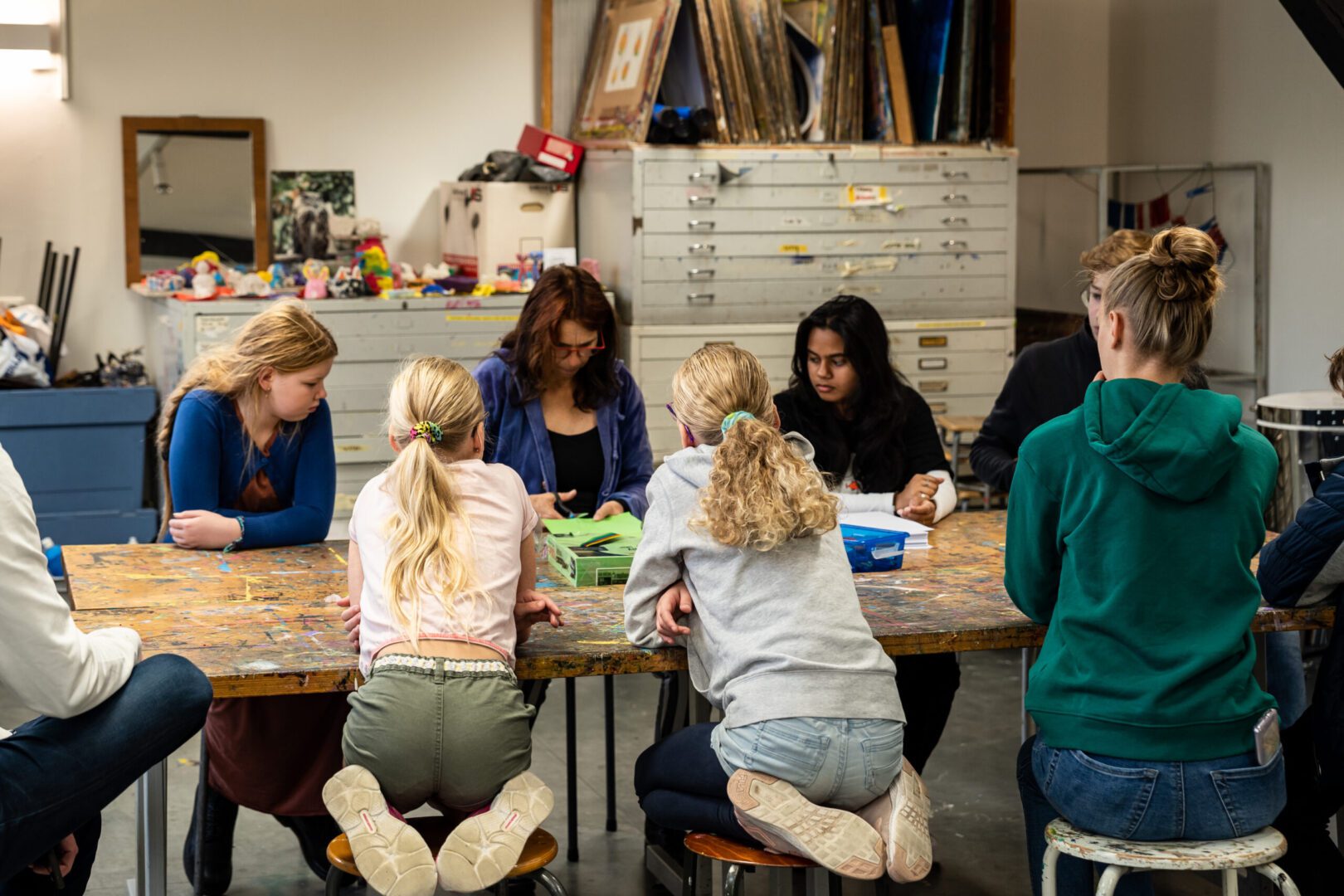 deelnemers van creatieve workshop textiel schilderen hangen over de tafel om de uitlegt van docent te zien